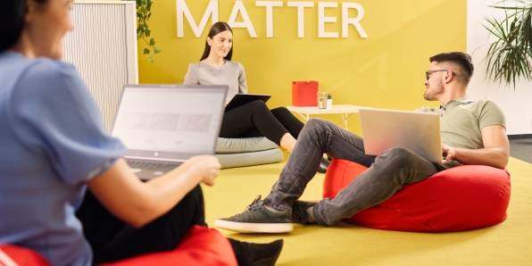 3 Mitarbeiter auf modernen Sitzsäcken im Loungebereich der IT sitzend. Alle haben einen Laptop auf den Knien.
