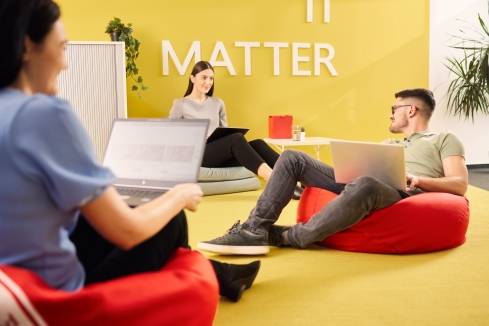3 Mitarbeiter auf modernen Sitzsäcken im Loungebereich der IT sitzend. Alle haben einen Laptop auf den Knien.