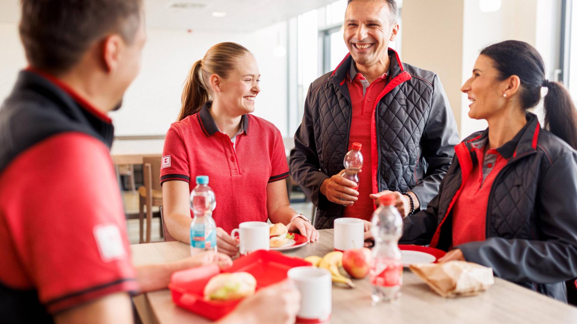 Vier Verkaufsmitarbeiter von Kaufland gut gelaunt bei der Mittagspause im Pausenraum eines Logistikzentrums.